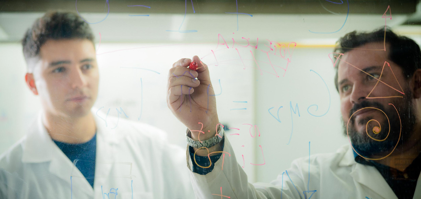 Research team working together to solve mathematical problems on a transparent board.